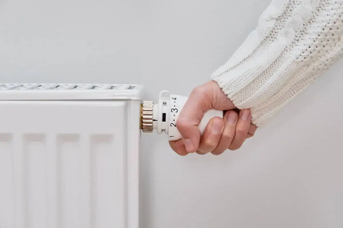 Mano ajustando el termostato de un radiador blanco. El dial está en un ajuste bajo, indicando que el radiador no calienta.
