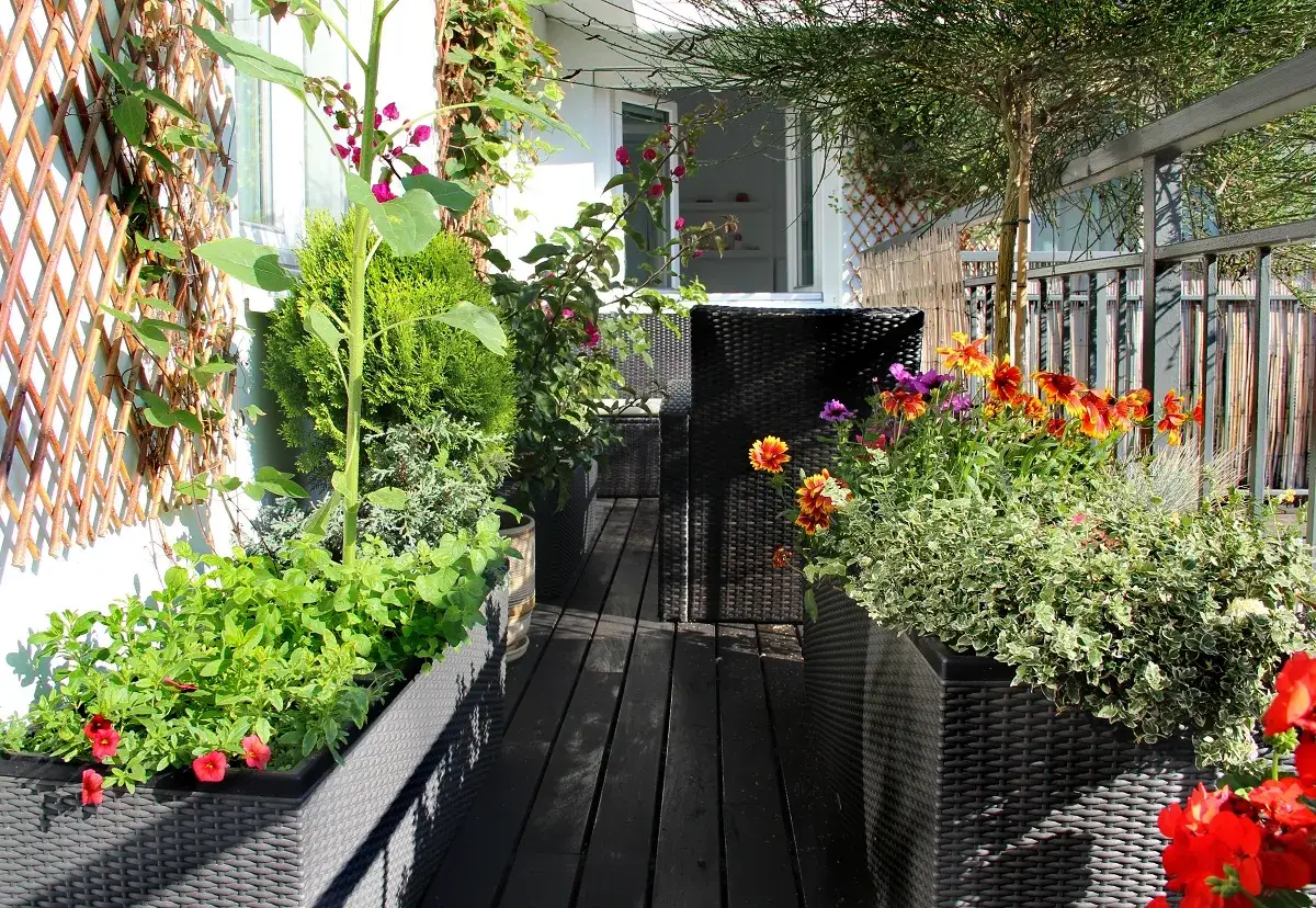 Un balcón convertido en un vibrante huerto en casa, con girasoles, flores de colores y plantas verdes en macetas.