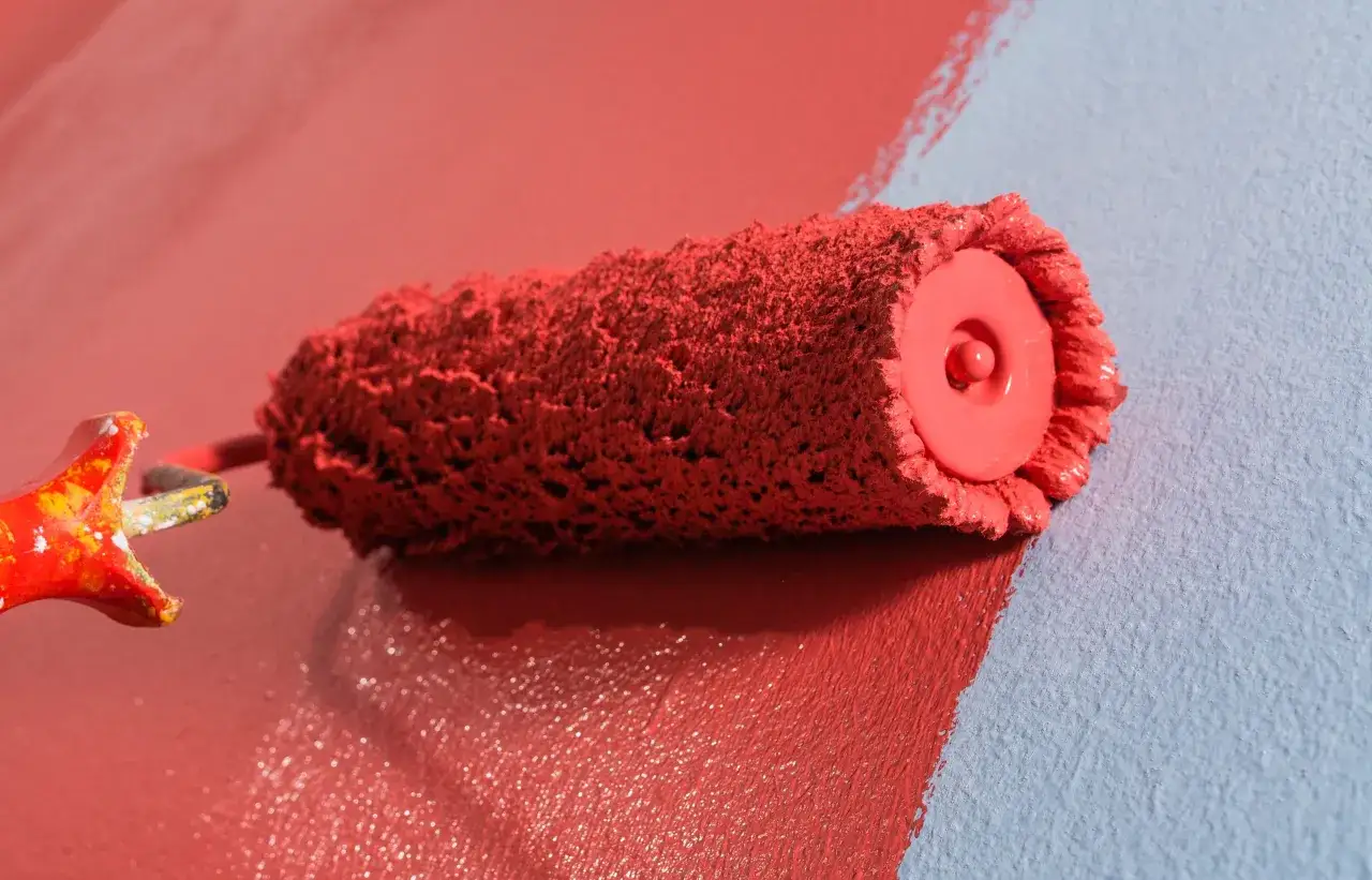 Rodillo de pintura roja dejando burbujas al pintar una pared azul.