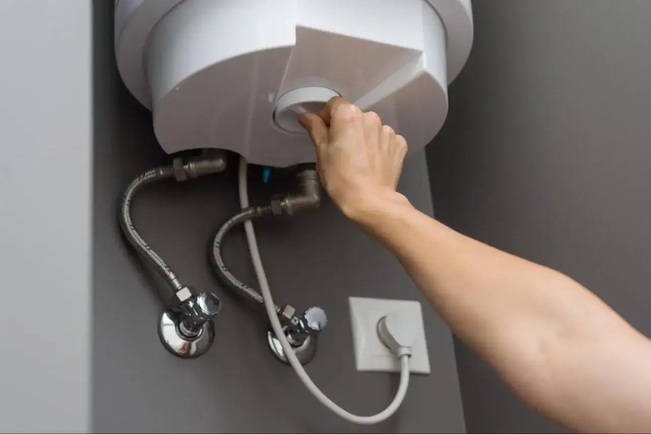 Mano girando el dial para cerrar la llave de paso del termo eléctrico.