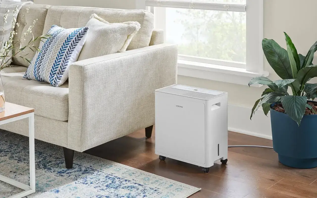 Un deshumidificador blanco moderno junto a un sofá beige, mostrando uno de los tipos de deshumidificadores para el hogar.
