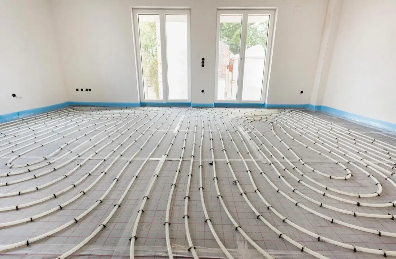Instalación de suelo radiante aerotermia en una habitación en construcción. Tubos blancos serpentean sobre una malla gris, listos para ser cubiertos.