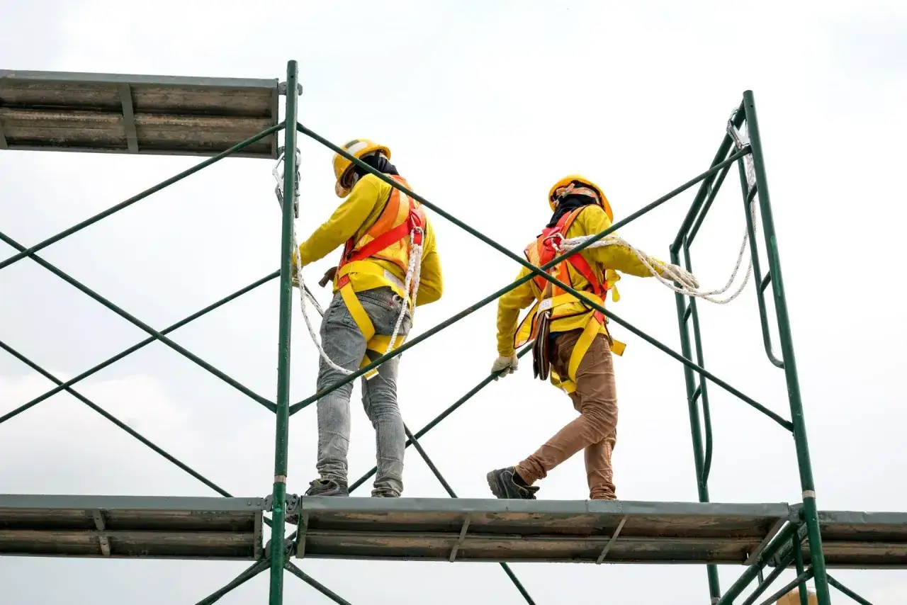 Dos trabajadores con arneses de seguridad en andamios, mostrando diferentes tipos de andamios en construcci&oacute;n.