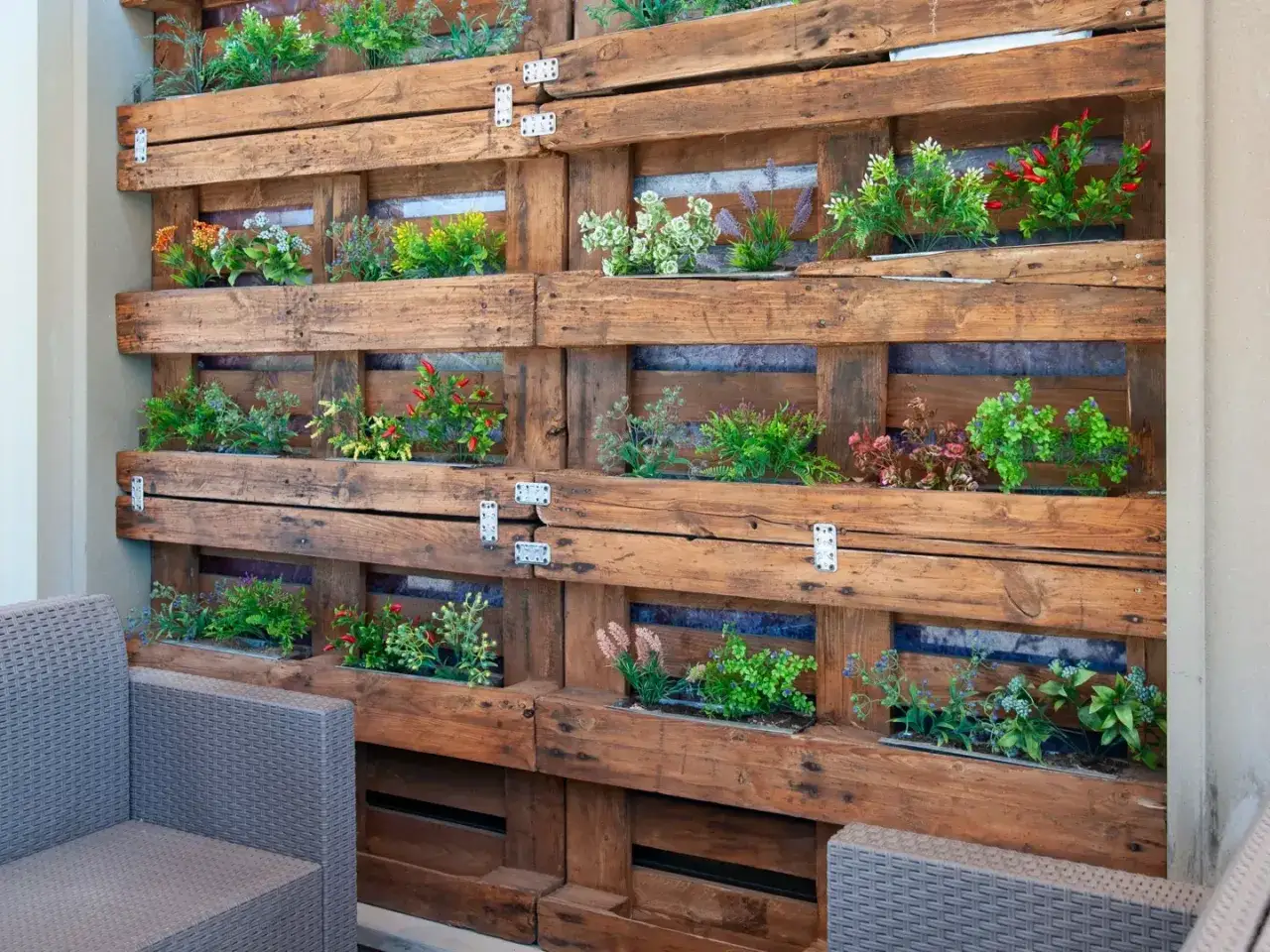 Un jardín vertical con palets exhibe plantas verdes y rojas en compartimentos de madera rústica, creando un oasis natural.