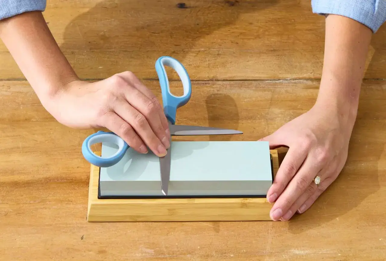 Manos afilando tijeras con piedra de afilar. Aprende cómo afilar tijeras con piedra para un corte perfecto.