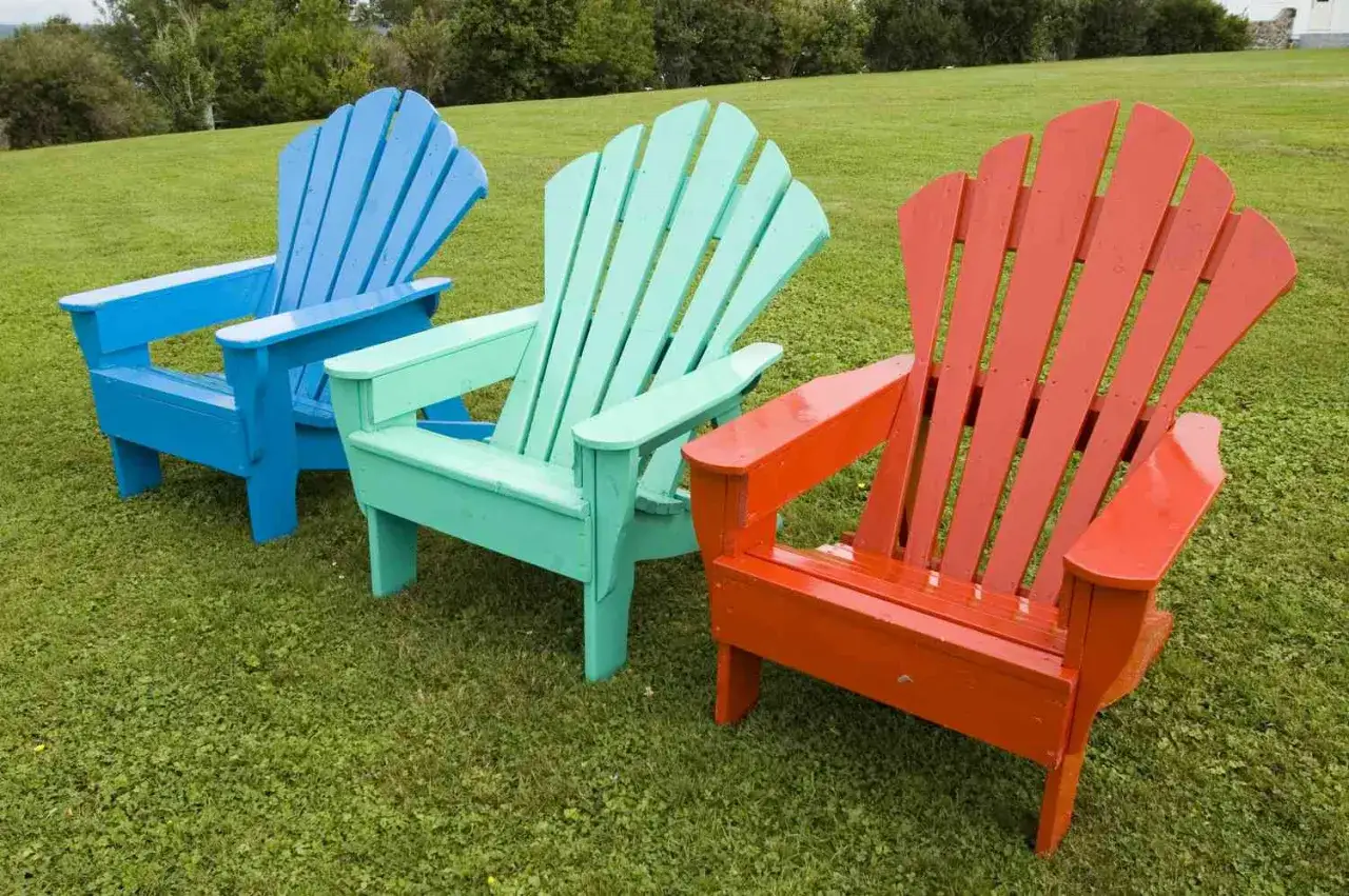 Tres sillas de madera de colores vibrantes (azul, verde menta y naranja) en el c&eacute;sped, listas para disfrutar del verano. &iexcl;Pintar sillas de madera sin lijar es f&aacute;cil y r&aacute;pido!