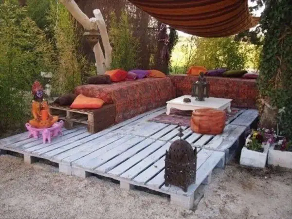 Un rincón zen con sofás y mesas bajas creados con jardineras con palets, cojines coloridos y faroles.